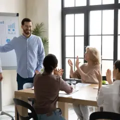 Dobry kierownik docenia zespół. Mężczyzna gratuluje pracownikowi, który prezentuje wykresy, a reszta zespołu klaszcze.