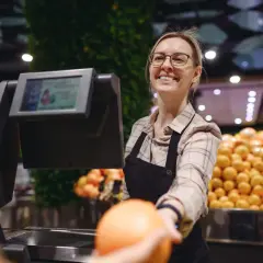 Uśmiechnięta kasjerka podaje pomarańczę. Czy to jeden z ostatnich takich zawodów, które znikną przez automatyzację?