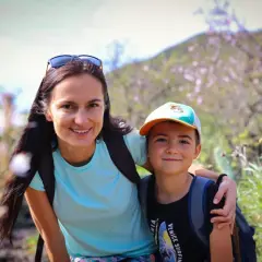 Uśmiechnięta mama z synem na tle kwitnącego wzgórza. "Jaka jestem? Taka, co kocha przygody i wspólne chwile.