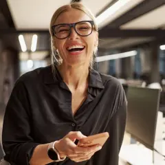 Uśmiechnięta kobieta w okularach trzyma telefon, inspirując się 7 nawykami skutecznego działania.