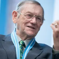 Starszy mężczyzna w okularach, z medalem na szyi i krawatem z pawimi oczkami, gestykuluje. Bo przecież nie myli się ten, co nic nie robi.