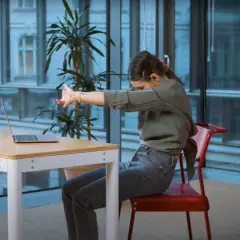 Kobieta siedząca przy biurku z laptopem wykonuje ćwiczenia rozciągające, by być aktywnie w pracy.