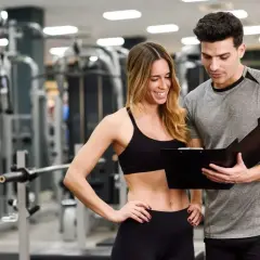 Trener personalny omawia plan treningowy z klientką na siłowni. Ich praca jako trenerów szkoleniowców przynosi efekty.