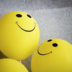 Żółte balony ze śmiejącymi się buźkami, symbolizujące pozytywną kulturę feedbacku i otwartą komunikację.