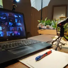 Laptop z ekranem pełnym twarzy uczestników online, mikrofon i notatki. Wirtualne spotkanie, które integruje zespół.