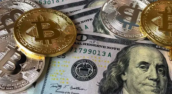 Złote i srebrne monety Bitcoin leżą na banknotach dolarowych. To obraz, który inspiruje do refleksji nad przyszłością pieniędzy i cytatami o finansach.