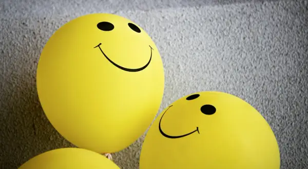 Żółte balony ze śmiejącymi się buźkami, symbolizujące pozytywną kulturę feedbacku i otwartą komunikację.