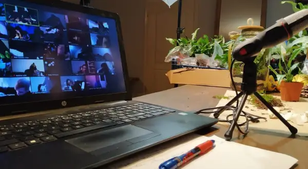Laptop z ekranem pełnym twarzy uczestników online, mikrofon i notatki. Wirtualne spotkanie, które integruje zespół.