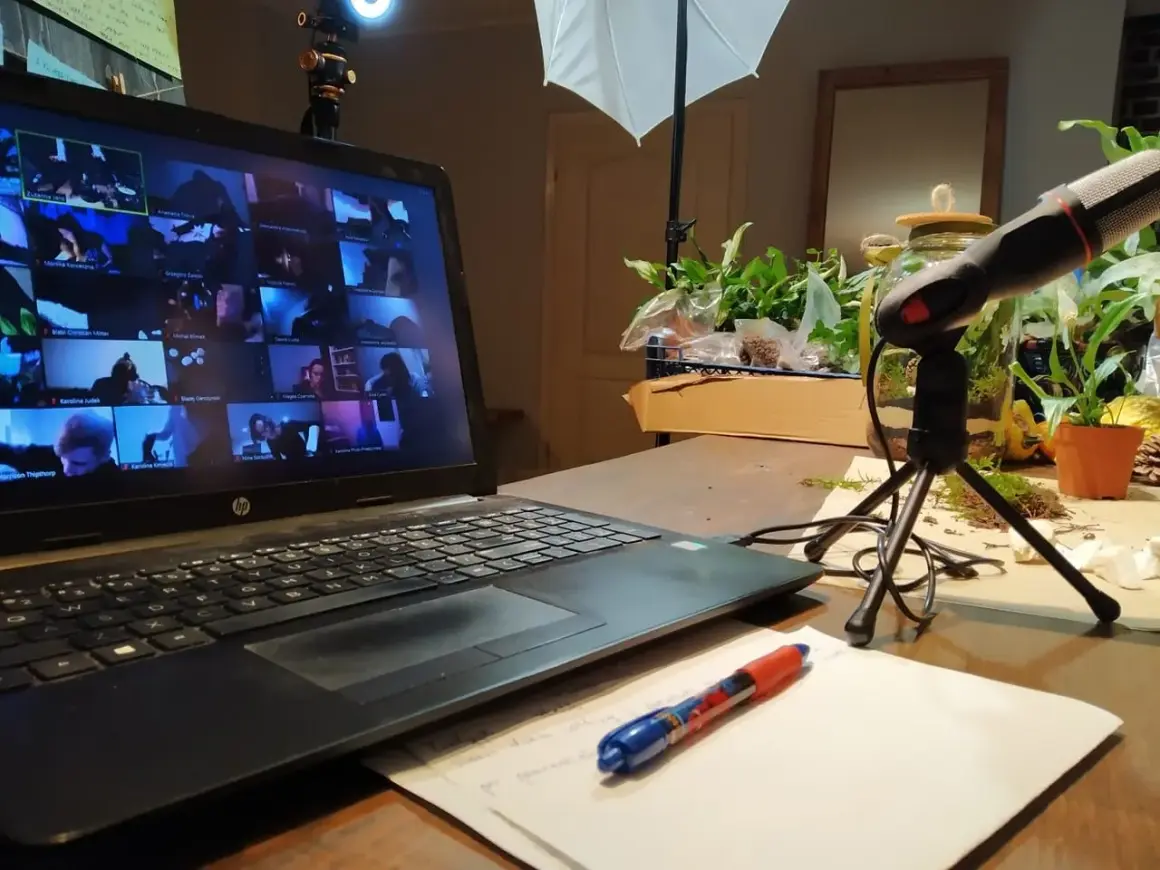 Laptop z ekranem pełnym twarzy uczestników online, mikrofon i notatki. Wirtualne spotkanie, które integruje zespół.
