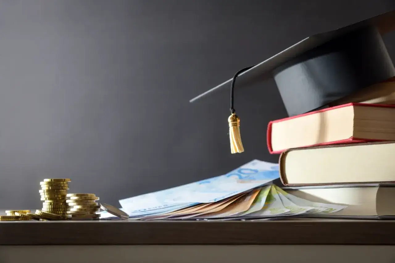Stos książek, czapka absolwenta i pieniądze. Czy warto iść na studia? Inwestycja w wiedzę.