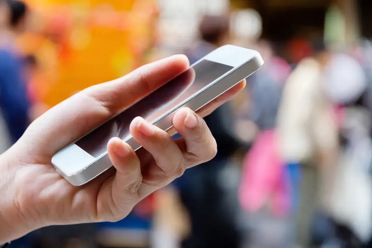 Dłoń trzyma smartfon, gotowa do wykonania telefonu. To Tw&oacute;j pierwszy krok, jak zapytać się o pracę przez telefon.